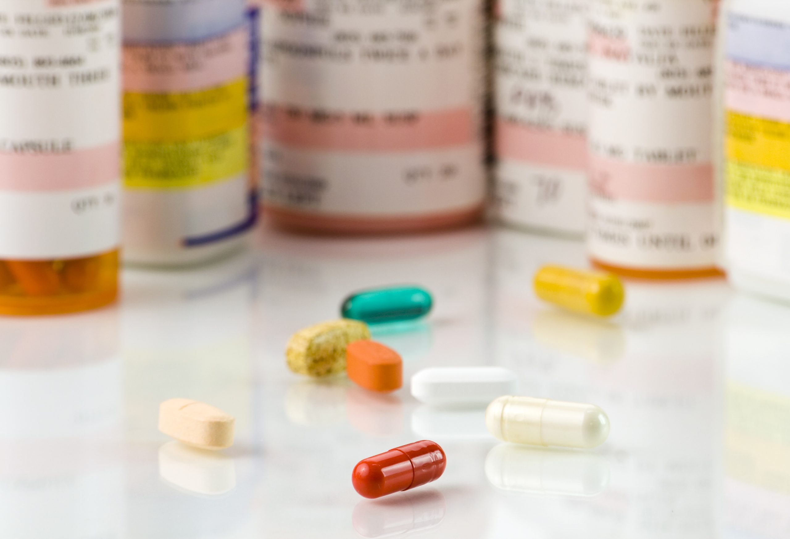 Close up of assorted pills and prescriptions on a high key background. The focus is on a front pill and falls off quickly